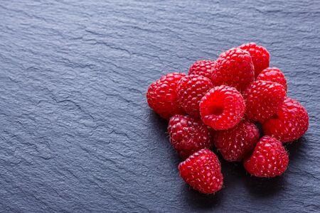 juicy fresh natural raspberries on a dark stone background.