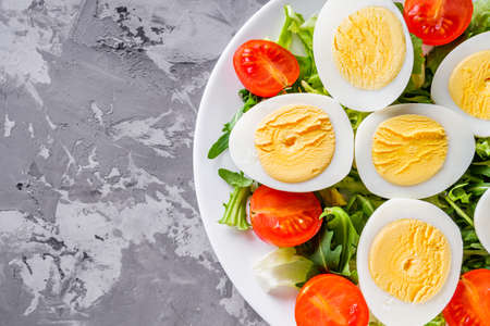 salad with boiled chicken eggs and cherry tomatoes on a stone background.の写真素材