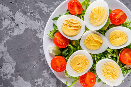 salad with boiled chicken eggs and cherry tomatoes on a stone background.
