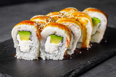 appetizing Philadelphia roll with eel and avocado on a black stone plate.