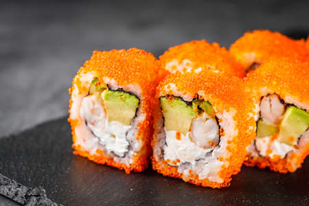 appetizing sushi roll california with avocado shrimp cheese and masago caviar on a black stone plate.の写真素材
