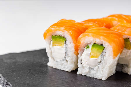 appetizing philadelphia roll with salmon and avocado on a black stone plate.