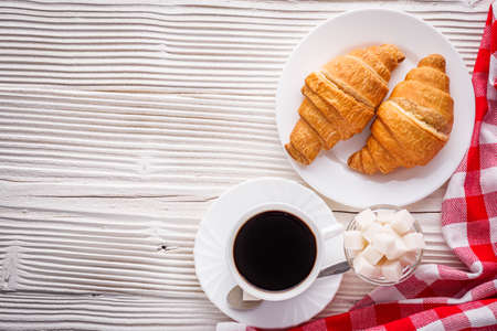 delicious fresh croissant and cup of coffee on a white wooden rustic background.