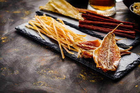 mug of beer and a set of dry fish snacks on a dark background.