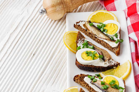 canapes with sprats on a white rustic wooden background.