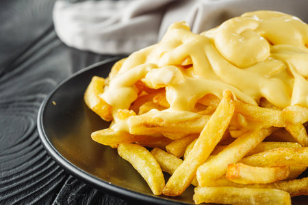 delicious crispy golden French fries with cheese on a black wooden rustic background.