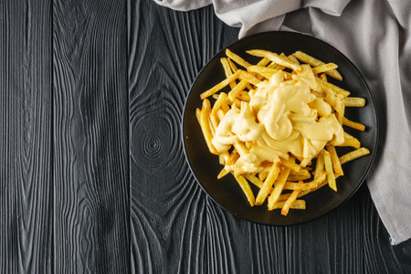 delicious crispy golden French fries with cheese on a black wooden rustic background.