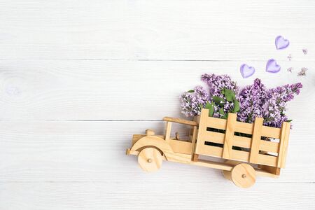 Wooden toy truck with lilac flowers in the back on white wooden background. Space for text. Festive greeting concept.の写真素材