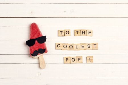 Father's Day greeting card with funny ice cream and wooden tiles comic text on white wooden background. To the coolest pop!の写真素材