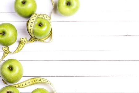 Green apples and yellow centimeter tape on white wooden background with space for text, top view. Concept sport, diet, fitness, healthy eating.の写真素材