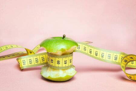 Green apple stump with yellow centimeter tape on pink  background. Concept sport, diet, fitness,...
