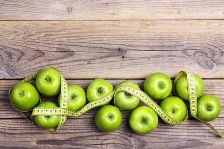 Green apples and yellow centimeter tape on old wooden background with space for text, top view. Concept sport, diet, fitness, healthy eating.の写真素材