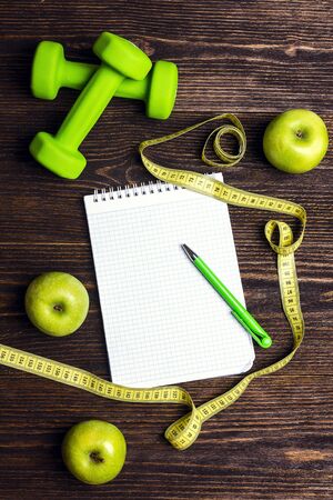 Open blank notepad with green dumbbells and green apples with measuring tape and copy space on wooden background. Sport, fitness and diet concept. Top view.の写真素材
