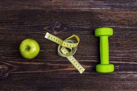 Green dumbbel, green apple and measuring tape on wooden background. Sport, fitness and diet concept. Top view.の写真素材