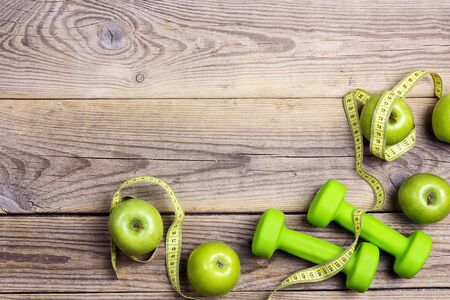 Green dumbbells and green apples with measuring tape and copy space on old wooden background. Sport, fitness and diet concept. Top view.の写真素材