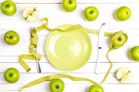 Diet concept table setting with cutlery, yellow measuring tape and green apples on white wooden table. Weight loss and healthy.の写真素材