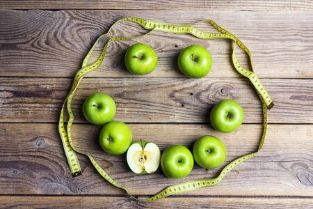 Smiling face of green apples and yellow centimeter tape on old wooden background. Apple dieting emoticon. Top view. Concept  diet and healthy eating.の写真素材