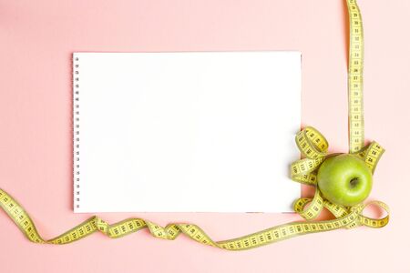 Blank open notebook with green apple and yellow centimeter tape on pink background with space for text. Concept sport, diet, fitness, healthy eating.の写真素材