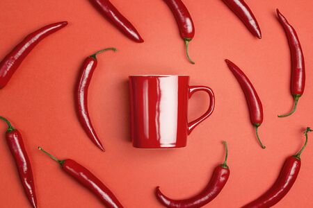 Red coffee mug surrounded by chili peppers on a red background. The concept of a hot drinkの写真素材