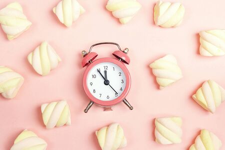 Pink alarm clock with colorful spiral marshmallows on pink background. Flat lay, top view.の写真素材