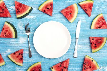 Summer table setting with cutlery and sliced watermelon on blue wooden table. Flat lay, top view, copy space.の写真素材