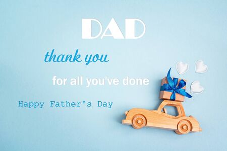 Father's Day greeting message with wooden toy car with a gift box on the roof on blue background. Fathers day background.の写真素材
