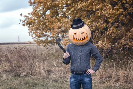 Jack-lantern with an ax and pumpkin on his head in a hat standing in the nature. Halloween legend.の写真素材