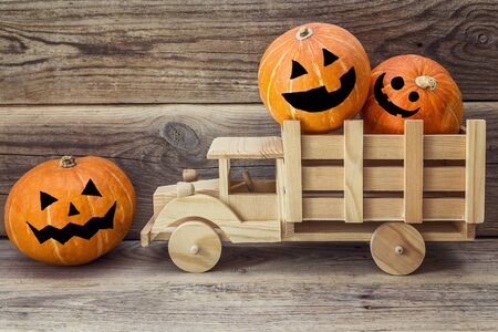 Wooden toy truck with Halloween pumpkins in the back on a background of old wooden boards.の写真素材