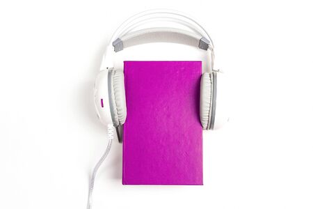 Purple book with a white  headphones on it on white background. Audio book concept. Top view with space for text.の写真素材
