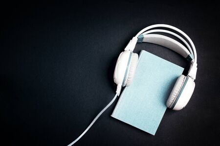 Blue book with a white  headphones on it on black background. Audio book concept. Top view with space for text.の写真素材