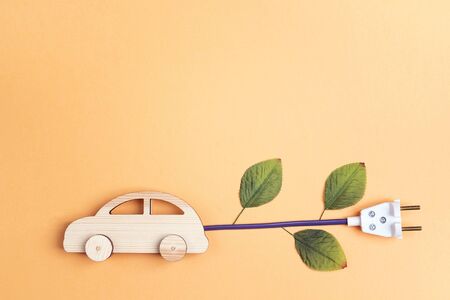 Wooden toy car with electrical cable plug with leaves as an electric car symbol. Save energy...