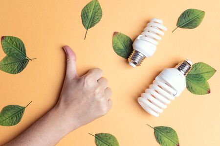Thumb up sign gesture hand and energy saving lightbulb. Ecology environment and saving energy concept. Flat lay, top view.の写真素材