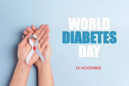 Helping hands holding blue ribbon awareness with red blood drop on a blue background. World diabetes day,14 november. Copy space, top view.の写真素材