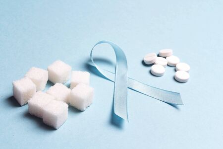 Blue ribbon with refined sugar and pills on a blue background. World diabetes day concept. Alternative to sugar for diabetics.の写真素材