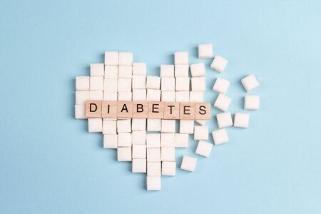 Broken heart made of sugar cubes with inscription diabetes on a blue background. World diabetes day concept.の写真素材