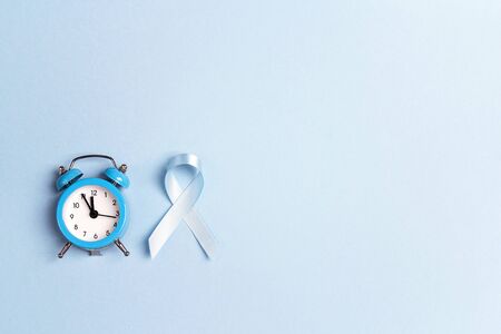 Blue ribbon awareness with alarm clock on a blue background. World diabetes day concept.