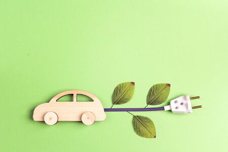 Wooden toy car with electrical cable plug as an electric car symbol. Save energy concept. Flat lay, copy space, top view.の写真素材