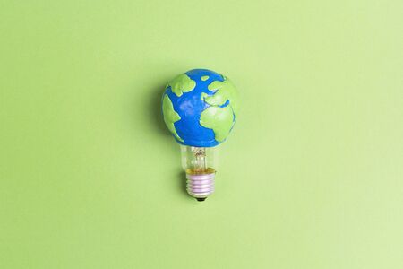 Light bulb with plasticine Earth planet model on green background. Global ecology, International Day of Energy Saving or Earth Hour concept.の写真素材