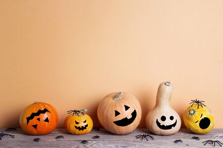 Halloween pumpkins with drawn funny faces on a wooden table on a orange background. Space for text.の写真素材