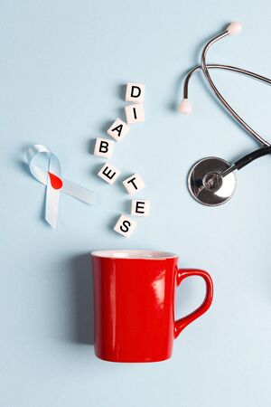 Red mug with sugar cubes, blue ribbon and stethoscope on a blue background. World diabetes day concept.の写真素材