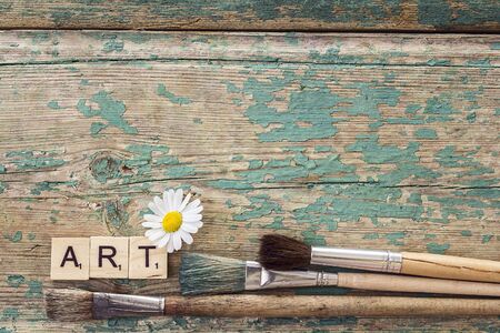 Background with  paintbrushes, chamomile, and the inscription art on old grunge boards. Copy space. Top viewの写真素材
