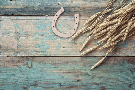 Background with ears of wheat and decorative horseshoe on old blue boards. Space for text.の写真素材