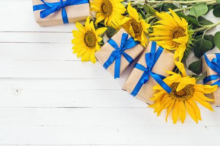 Background with a bouquet of yellow sunflowers and gift boxes with blue ribbons on a white painted wooden planks. Space for text.の写真素材