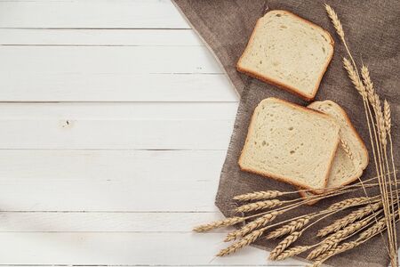 Slices of white bread and wheat ears on sacking on white boards. Space for text.
