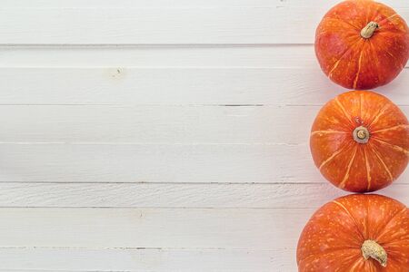 Background with three small orange pumpkins on a white wooden boards. Space for text. View from...