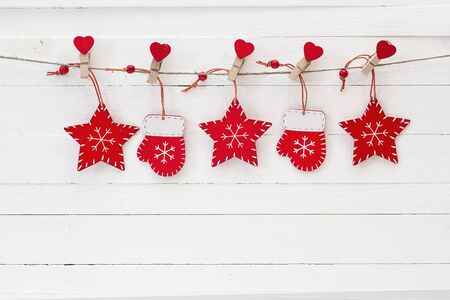 Red Christmas decorations hanging on clothespins on a white wooden background. Space for text.
