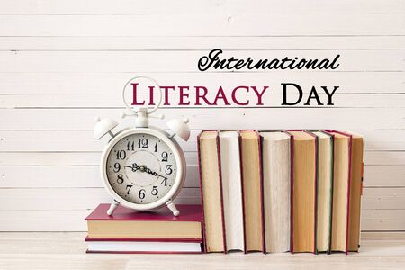 International Literacy Day concept with alarm clock and pile of books on white wooden table.の写真素材