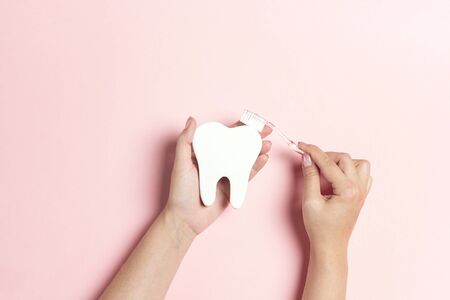 Female hands with tooth symbol and toothbrush on pink background. Dental health, brushing and whitening teeth concept. Flat lay, top view, copy space.の写真素材