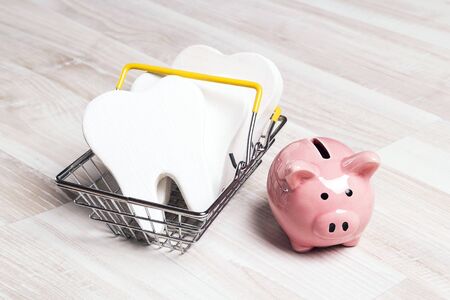 Pink piggy bank with teeth in shopping basket on a light wooden background. Investing in dental health care.の写真素材