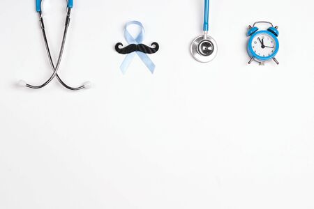 Blue ribbon with mustache, stethoscope, alarm clock and copy space on white background. Prostate cancer awareness. Men healthcare.の写真素材